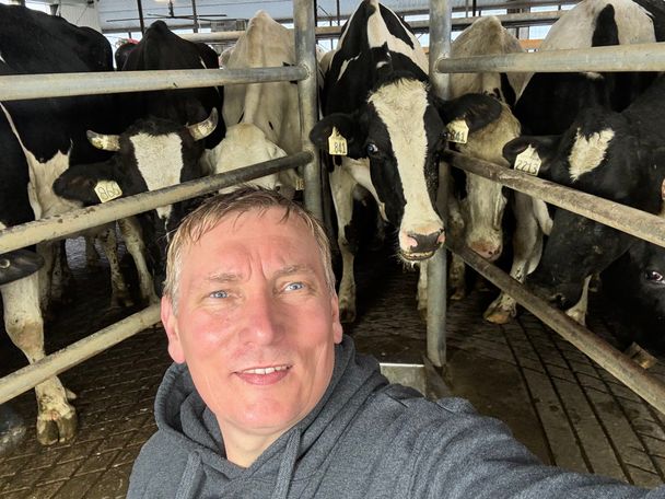 Smiling team member takes a selfie with curious Holstein dairy cows behind galvanized pen gates after a barn wash