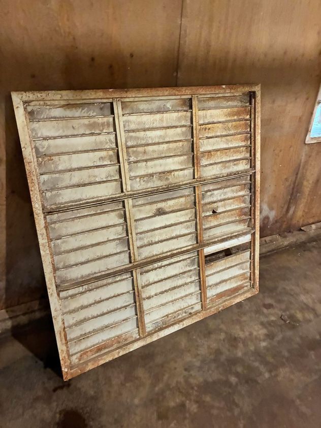Barn fan louvre shutter caked in dust and rust-brown grime, removed from the fan wall before cleaning