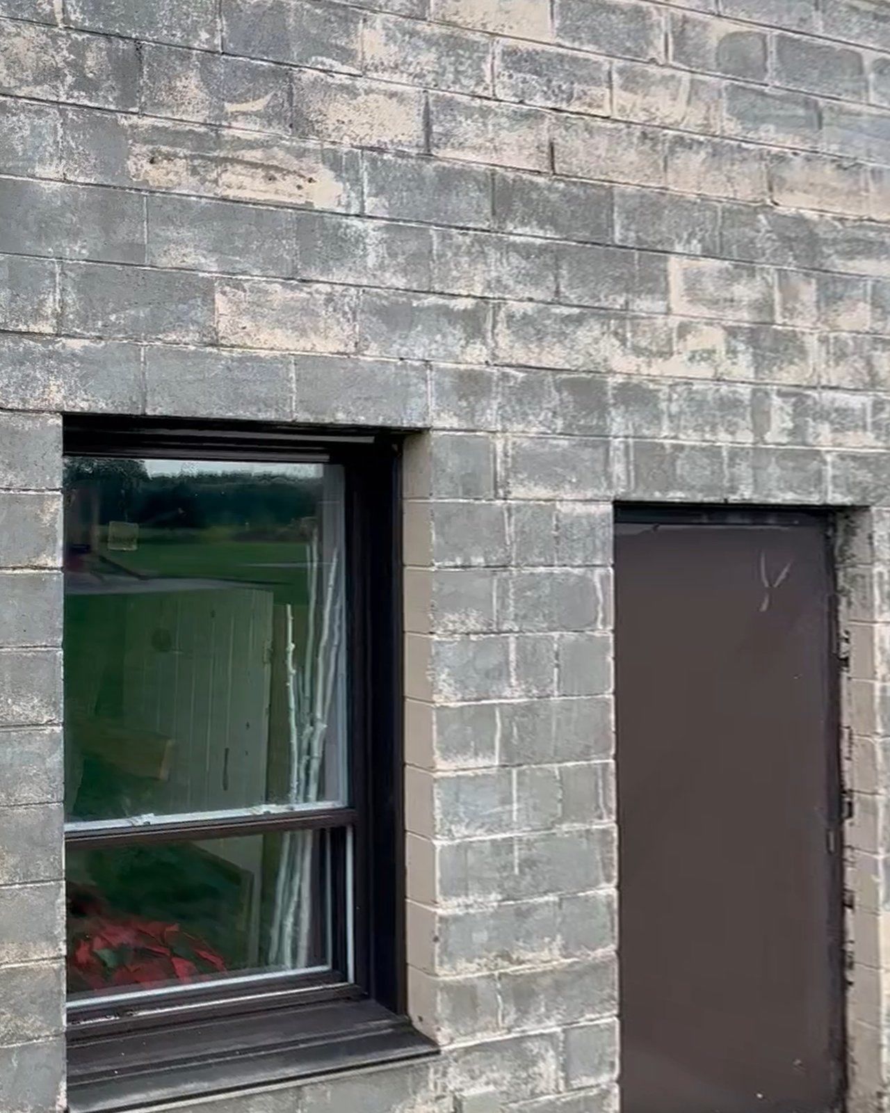 The same section of wall that evening after a paint-stripping pass: mostly bare grey block, with traces of white paint left in the joints and on some blocks.