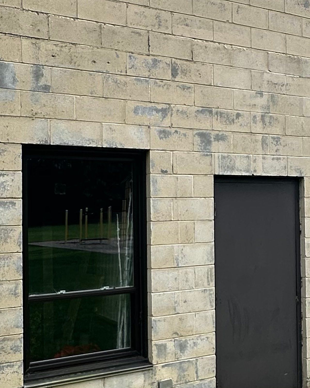 Concrete block wall of a barn before paint removal: cream paint peeling off in grey patches around a dark window and a dark door.