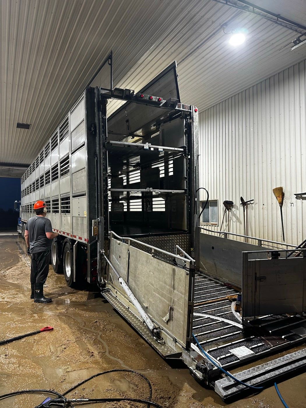 A washed triple-deck hog trailer in a wash bay, a crew member in a hard hat looking it over