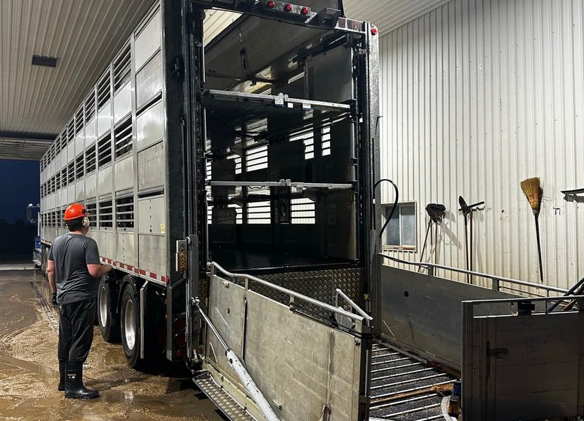 A washed triple-deck hog trailer in a wash bay, a crew member in a hard hat looking it over