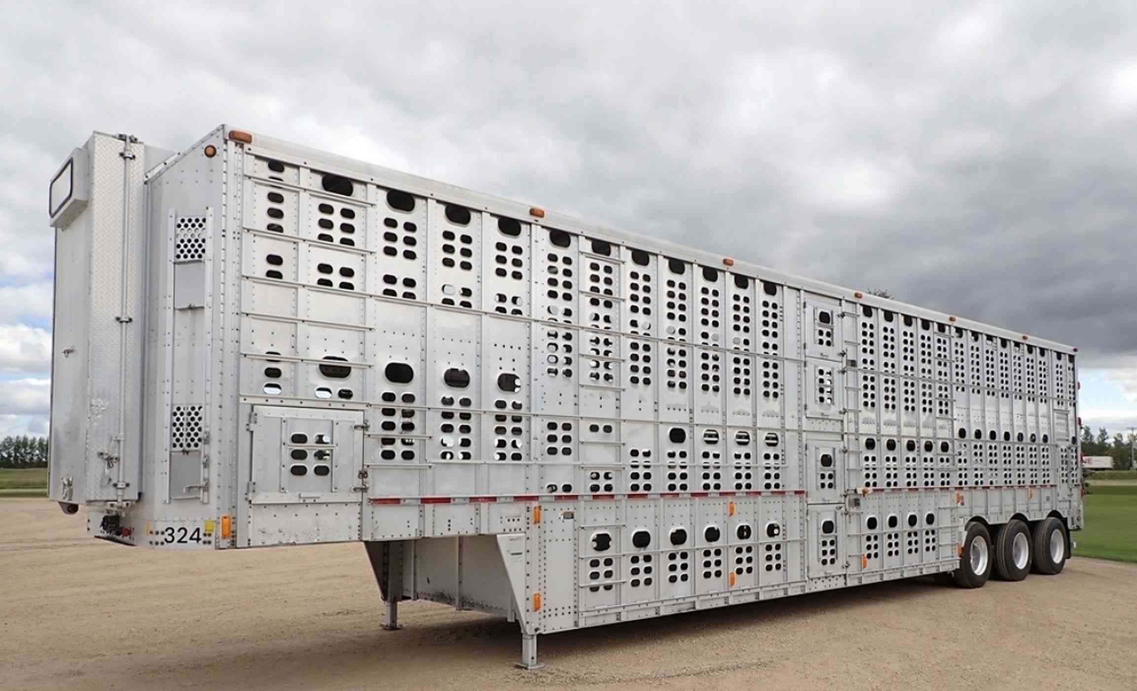 A multi-deck aluminium livestock trailer parked on a gravel yard under a cloudy sky
