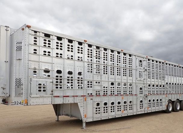 A multi-deck aluminium livestock trailer parked on a gravel yard under a cloudy sky