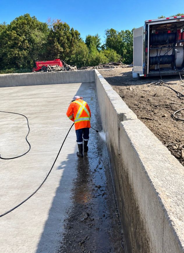 Crew member pressure-washing manure staining off the base of a concrete pit wall during a Norfolk County pit cleanout