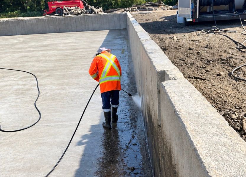 A crew member pressure washing the dark manure line off the base of a concrete pit wall