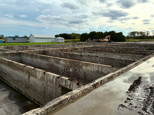 Concrete manure storage cells with dark manure staining on the walls and wet sludge along the edge, still to be washed