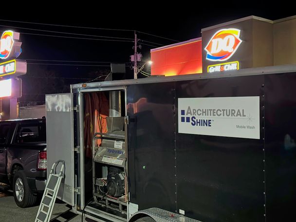 The Architectural Shine Mobile Wash trailer at night beside a Dairy Queen, side door open on the pressure washer inside, with the pickup that tows it
