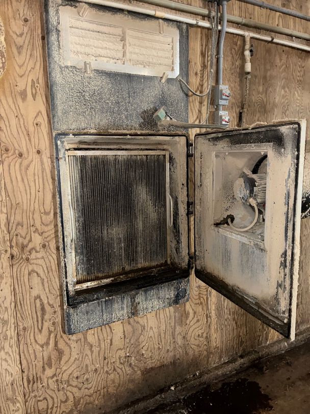 Dust-caked hot-water heater opened for cleaning in a poultry barn, coil and fan motor coated in barn dust