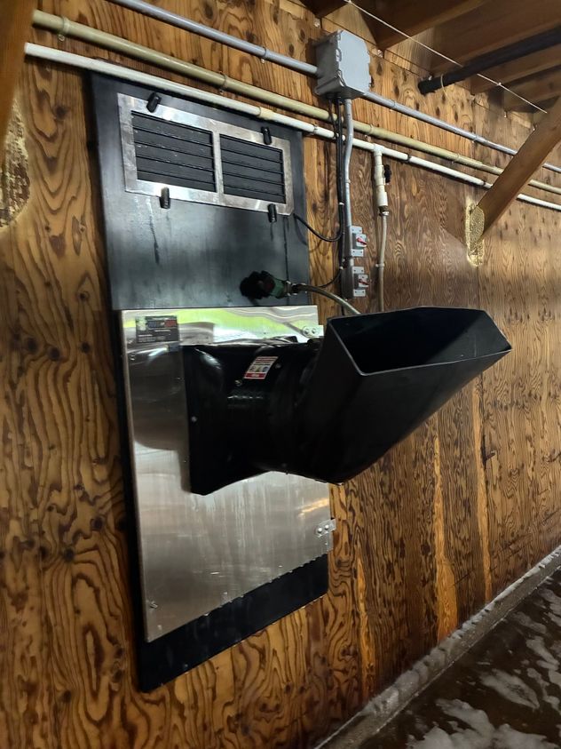 Cleaned hot-water heater with stainless panel and black discharge nozzle on a freshly washed poultry barn wall