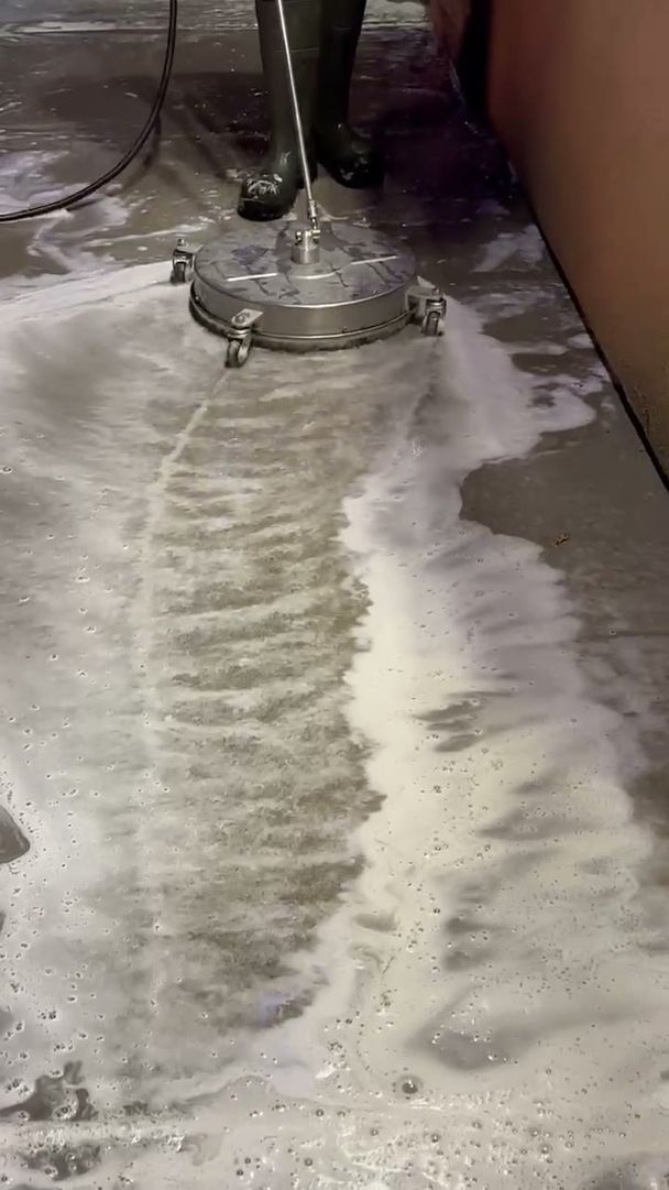 Concrete walkway mid-wash with clean stripes left by a surface cleaner beside dirty, soapy concrete
