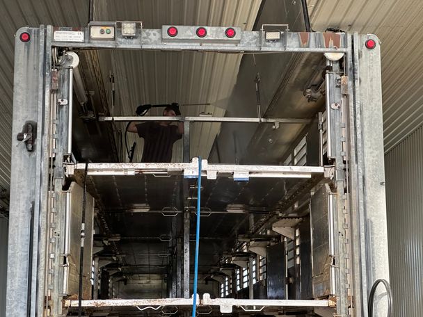 Pressure washing the top deck of a multi-deck swine transport trailer, spray mist visible in a truck wash bay